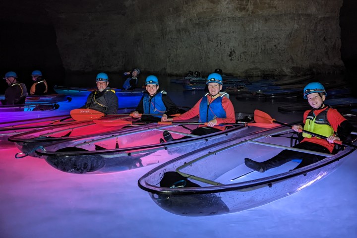 A group of kayakers pose side-by-side in the Gorge Underground in Crystal Clear Kayaks surrounded by the colorful illumination of underwater LEDs.