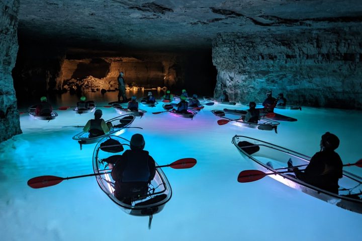 A group of kayakers tour the Gorge Underground in Crystal Clear Kayaks surrounded by the colorful illumination of underwater LEDs.
