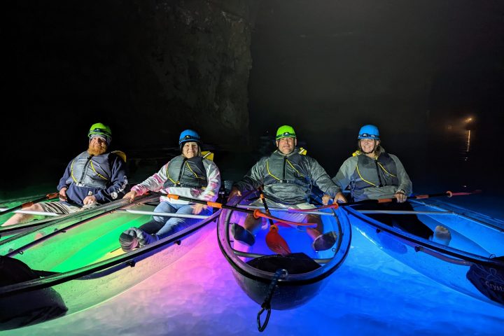 A group of Crystal Clear Kayaks are positioned side-by-side and are surrounded by the colorful illumination of underwater LEDs.