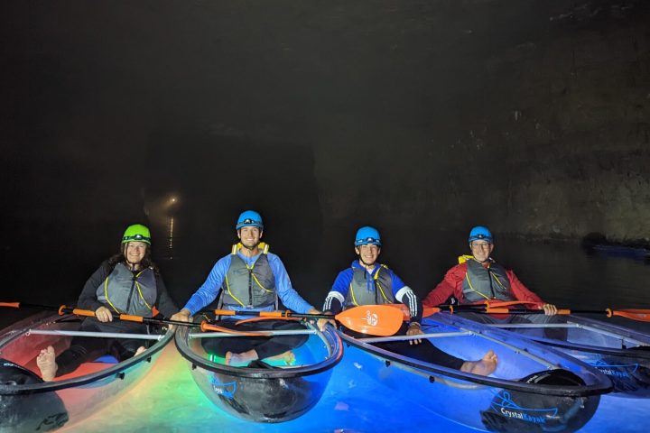 A group of Crystal Clear Kayaks are positioned side-by-side and are surrounded by the colorful illumination of underwater LEDs.