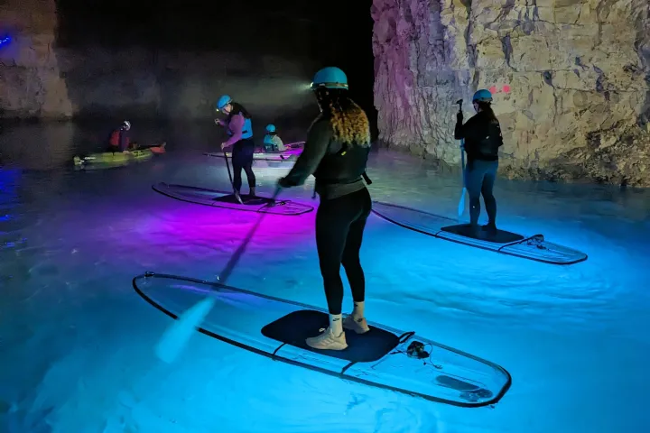 People paddleboarding in an illuminated cave with colorful lights.