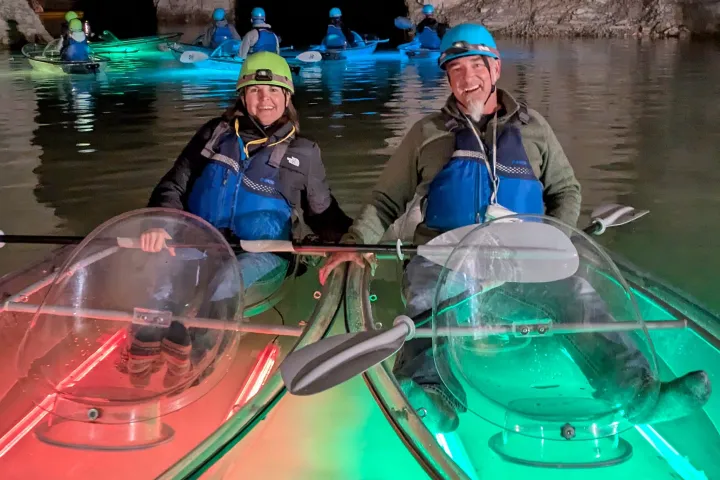 Two people kayaking with colored lights in a cave.