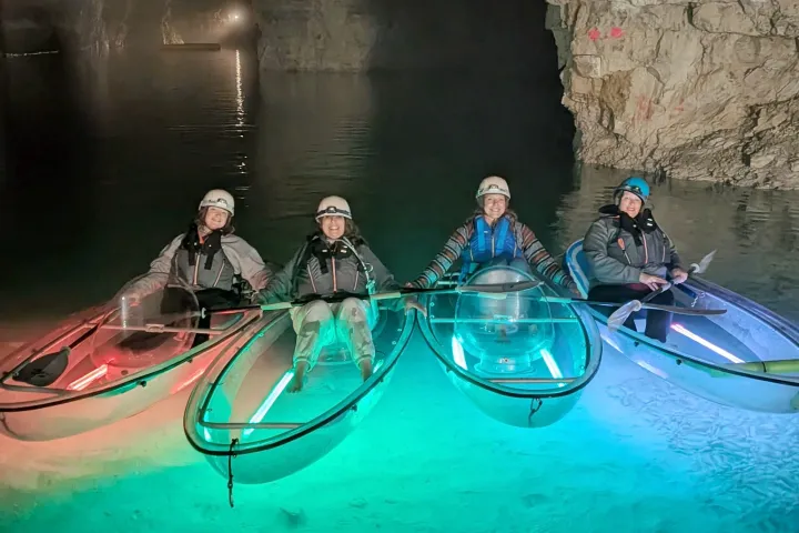 Four people in illuminated kayaks inside a dimly lit cave.