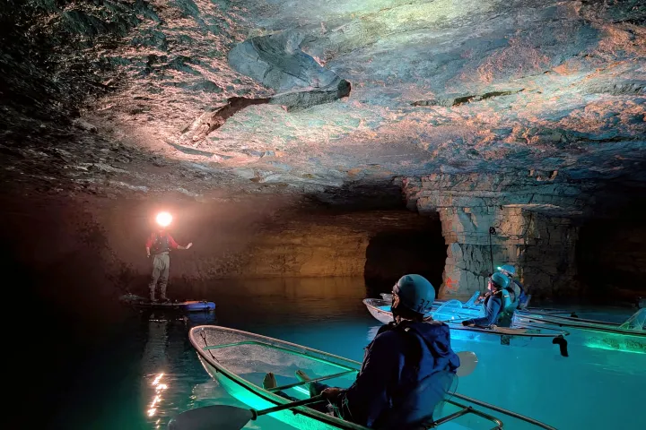 People in transparent kayaks exploring an illuminated cave.