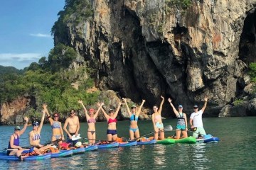 a group of people riding on the back of a boat in the water with Railay Beach in the background